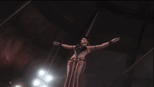 a woman in a red and white striped outfit is standing on a red and yellow item with her arms outstretched