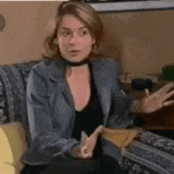 a woman is sitting on a couch wearing a choker and a jacket .
