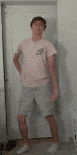 a man in a pink shirt and shorts is standing in front of a door .