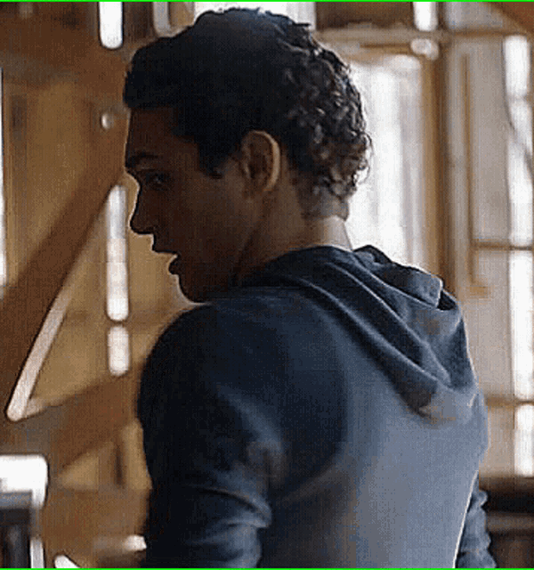 a man with curly hair wearing a blue hoodie is looking over his shoulder .