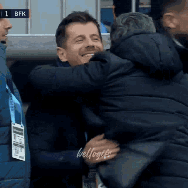 a man in a black jacket hugging another man in a black jacket