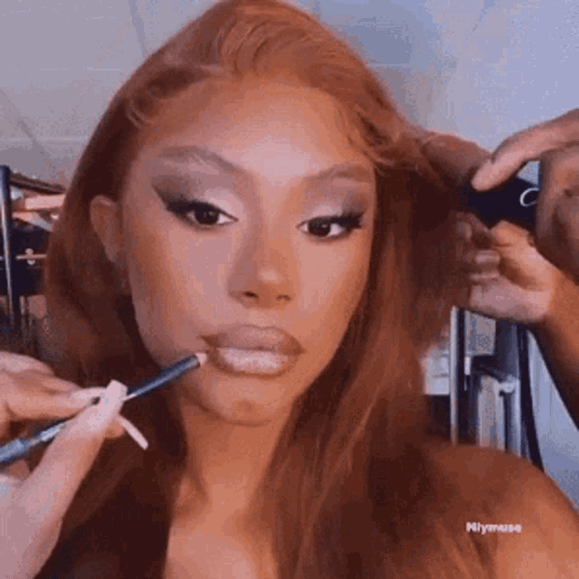 a woman with long red hair is getting her makeup done .