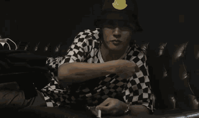 a man wearing a black hat and a checkered shirt is sitting on a couch