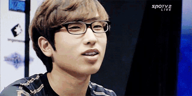a young man wearing glasses is smiling in front of a sign that says spotv2 live