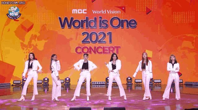 a group of women are dancing on stage in front of a sign that says world is one 2021 concert