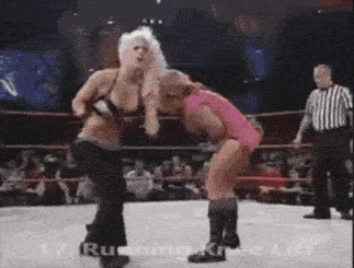 two women are wrestling in a wrestling ring with a referee watching .