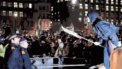 a woman in a blue jacket stands in front of a crowd holding a flag with a sign that says " i love cu "