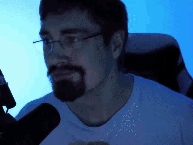 a man with glasses and a beard is sitting in front of a blue background