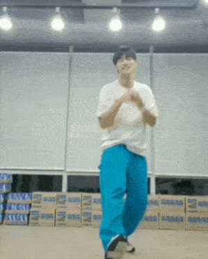 a man in a white shirt and blue pants is dancing in a room in front of boxes .