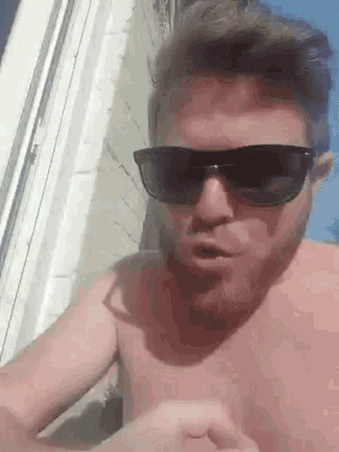 a shirtless man with a beard is wearing sunglasses and talking .