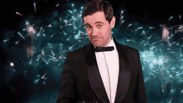 a man in a tuxedo is standing in front of a fireworks display