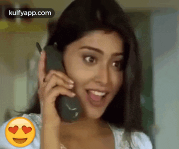 a woman is talking on a cell phone with a heart shaped emoji in her eyes .