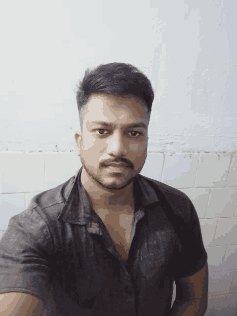 a man with a beard is taking a selfie in front of a white tiled wall