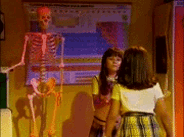 two girls are standing in front of a skeleton .