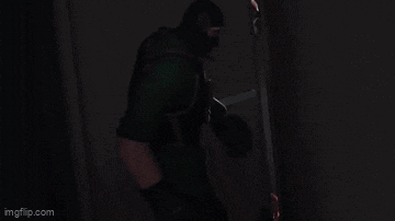 a man in a green uniform is standing in a dark room with a gun .