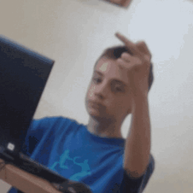 a boy in a blue shirt is giving the middle finger in front of a laptop