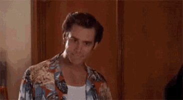 a man in a hawaiian shirt is standing in front of a wooden wall and saying `` alright then ! ''