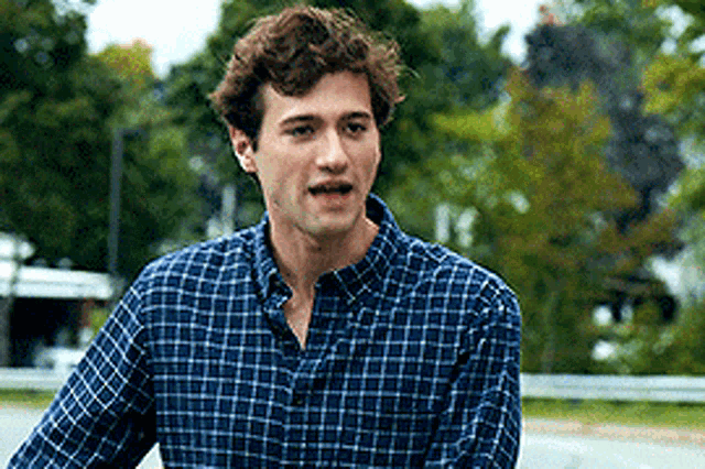 a young man wearing a blue plaid shirt is standing on a street .