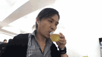 a woman in a plaid shirt is drinking a cup of liquid .