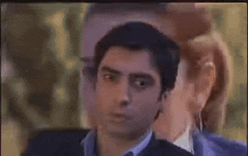 two men are standing next to each other in a room and one of them is whispering into the other 's ear .