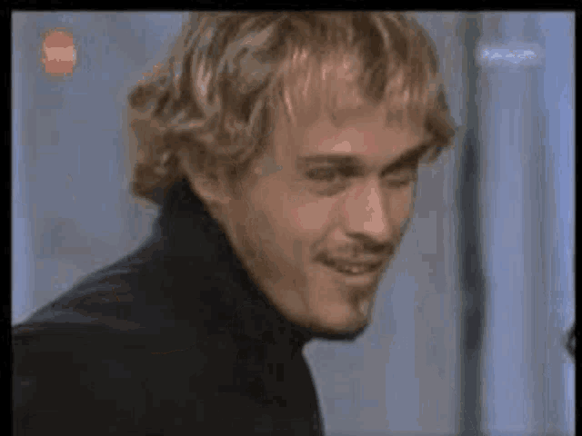 a man with blonde hair and a beard is smiling and looking at the camera .