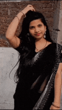 a woman wearing a black saree is standing in front of a brick wall .