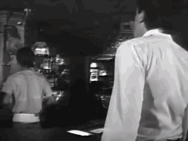 a man in a white shirt is standing in front of a counter in a restaurant .