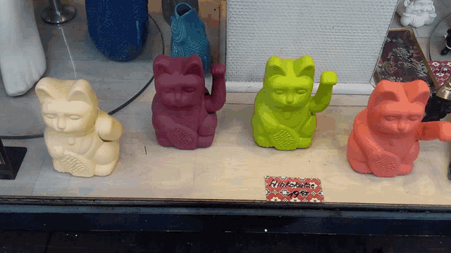 four different colored cats are sitting on a table with a sign that says nikkeicafe on it