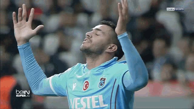 a soccer player wearing a blue vestel jersey with his hands up in the air