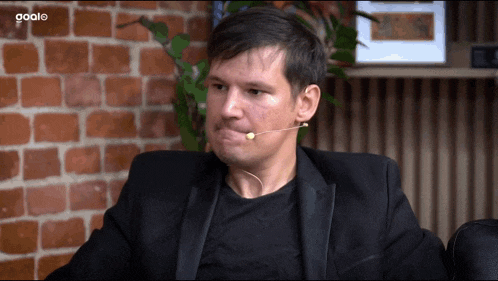 a man with a microphone in his mouth sitting in front of a brick wall