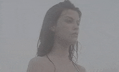 a woman in a bikini is standing in the fog looking at the camera .
