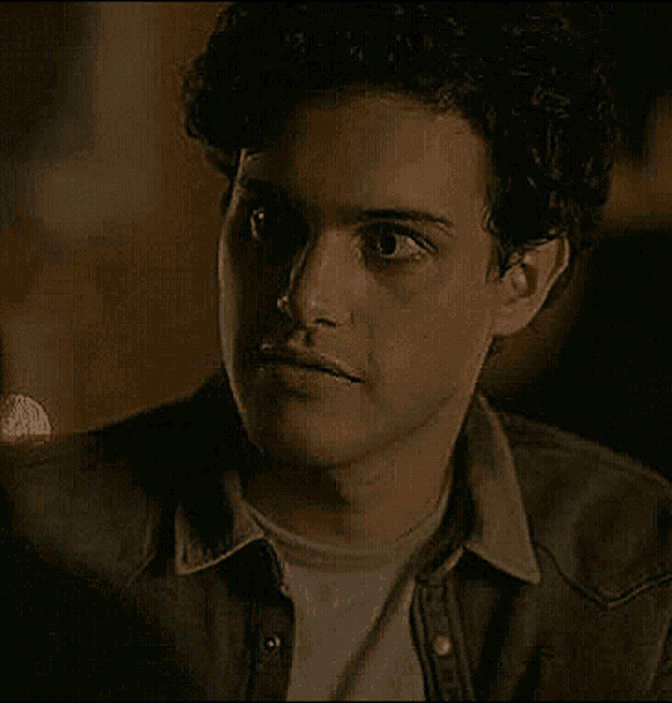 a close up of a young man with curly hair wearing a denim jacket and smiling .