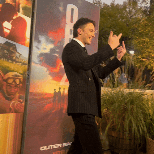a man in a suit stands in front of a poster that says outer bay