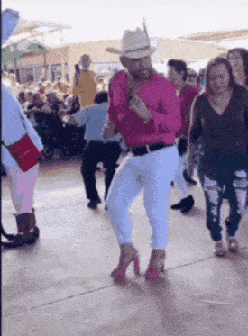 a man in a pink shirt and white pants is dancing in a crowd