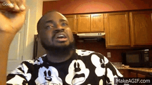 a man wearing a mickey mouse shirt is making a funny face in a kitchen