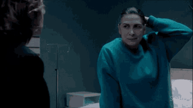 a woman in a blue sweater is talking to another woman in a hospital room and says a ganging