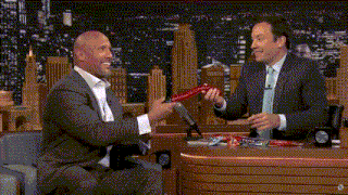 two men are sitting in front of a microphone and one of them is holding a red object in his hand .