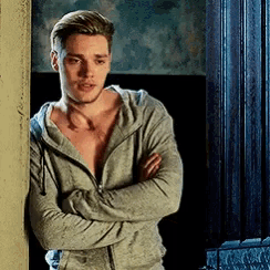 a shirtless man is leaning against a wall with his arms crossed and looking at the camera .