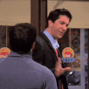 a man in a suit and tie talking to another man in front of a sign that says extra