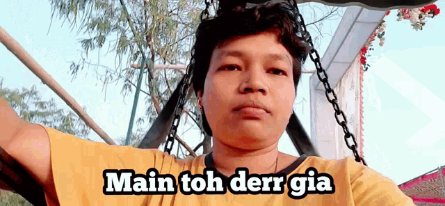 a man in a yellow shirt is sitting on a swing with the words main toh derr gia below him
