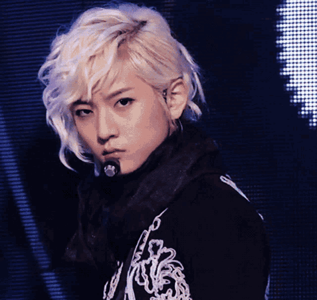 a young man with blonde hair is wearing a black jacket with the letter r on the front