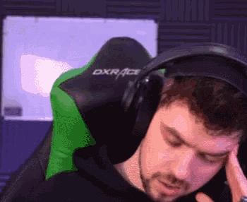 a man wearing headphones is sitting in a green chair and holding his head .
