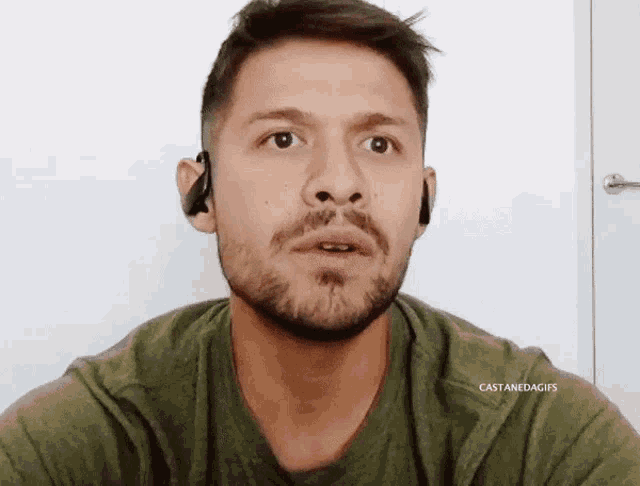 a man with a beard is wearing a green shirt and earbuds .