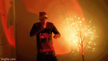 a man in a santa hat is dancing in front of a christmas tree with lights