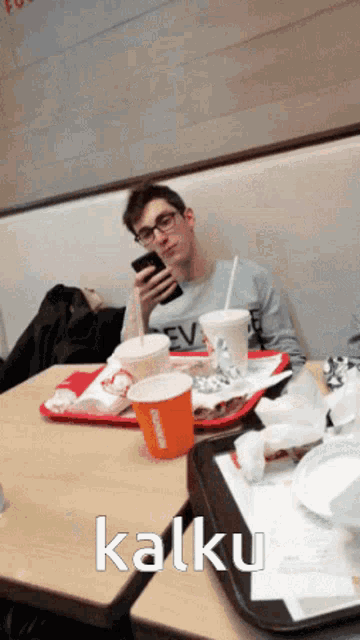 a man sits at a table with a tray of food and drinks and looks at his phone