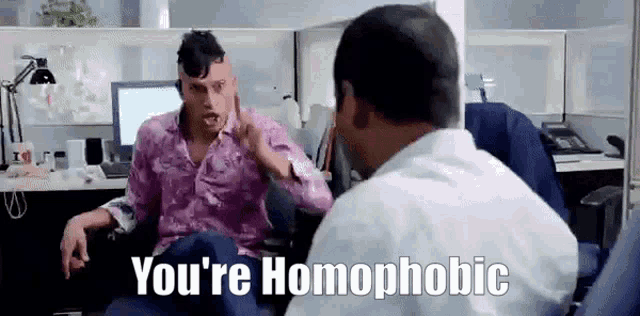 a man in a pink shirt is talking to a man in a white shirt who is sitting in a chair .