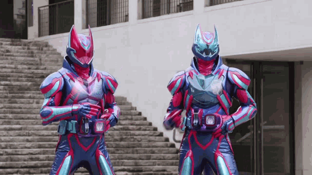 two kamen riders are standing next to each other on a set of stairs in front of a building .