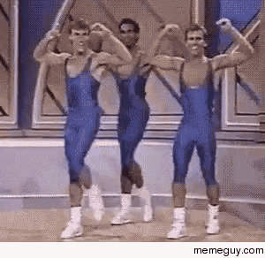three men in blue overalls are flexing their muscles in a room .