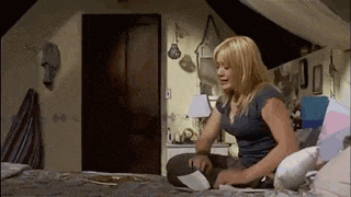 a woman is sitting on a bed in an attic room looking at a piece of paper .