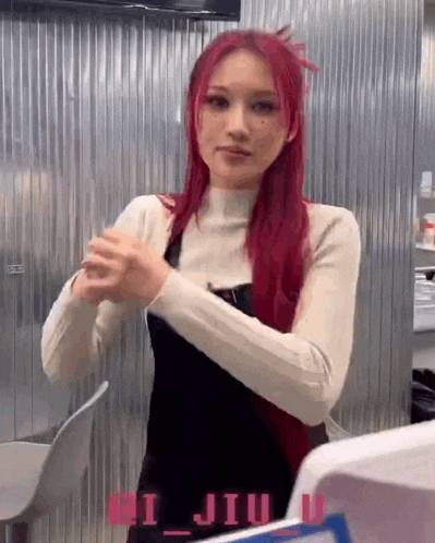 a woman with red hair is standing in front of a metal wall with her hands folded .